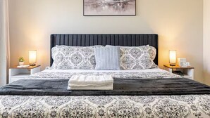 A neatly arranged hotel room with a large bed, a headboard, two bedside tables with lamps, a clock, and a framed picture on the wall. - Quiet Comfort-Parking & Patio • WiFi • WD (Austin)