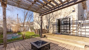 A covered patio with a wooden deck, a glass table, and a metal bench. - Quiet Comfort-Parking & Patio • WiFi • WD (Austin)