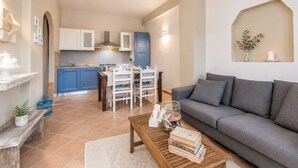 Ein Wohnzimmer mit einer Couch, einem Couchtisch mit Büchern, einem Essbereich mit Stühlen und einem Tisch sowie einer Küche mit Schränken und einem Herd.