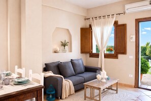 A cozy living room with a grey sofa, a wooden coffee table, and a dining area with a white table and plates.