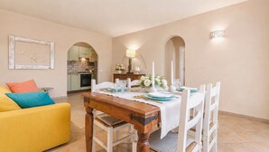 A dining area with a wooden table, white chairs, and a yellow sofa. - Dimora Acquamarina, Baja Sardinia, Italy (Baja Sardinia)
