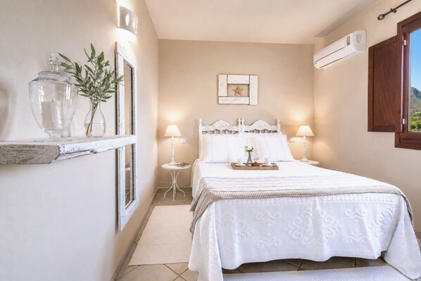 Un dormitorio con cama, lámparas de noche, mesita de noche, espejo, aire acondicionado instalado en la pared y ventana con vista.