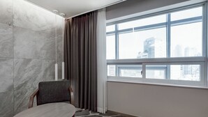 A hotel room with a large window, a marble wall, a round table, and a chair.