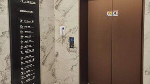 An elevator with a marble wall and a black information panel listing floors and amenities.