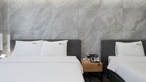 A hotel room with two beds, each with a white bedspread and pillows labeled "Hayton". There is a wooden nightstand with a phone and a small table between the beds.