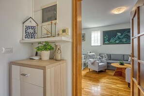 Sala de estar moderna com piso de madeira, um sofá cinza, uma mesinha e uma planta sobre um console de madeira.