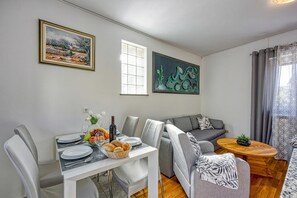 A dining area with a table set for four, a grey sofa, and two framed artworks on the wall.