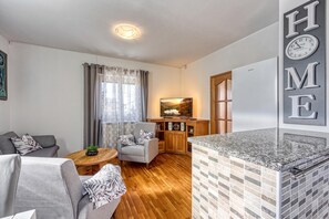 A modern living room with a sofa, armchair, and a small table with a plant. There is a painting on the wall and a kitchen area with a countertop and backsplash. - Jakara Sweet Escape 5, Vinkuran, Croatia (Vinkuran)