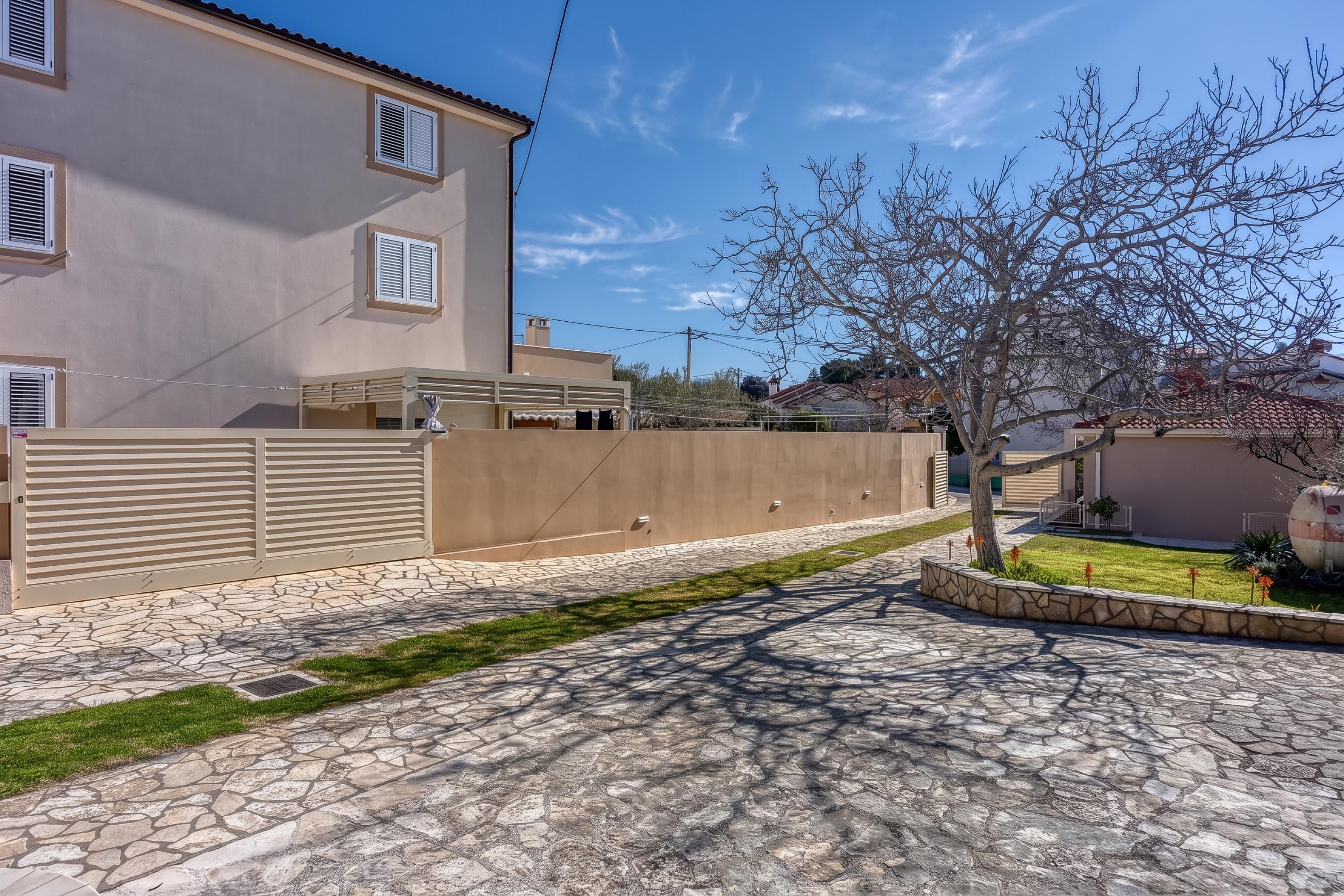 Una propietat residencial amb una entrada asfaltada, una zona tancada i un arbre.