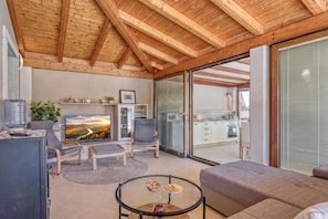 A modern living room with a TV, seating, and a glass door leading to a kitchen.