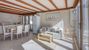 En rummelig opholdsstue med træloft, spisebord med stole, sofa og sofabord.