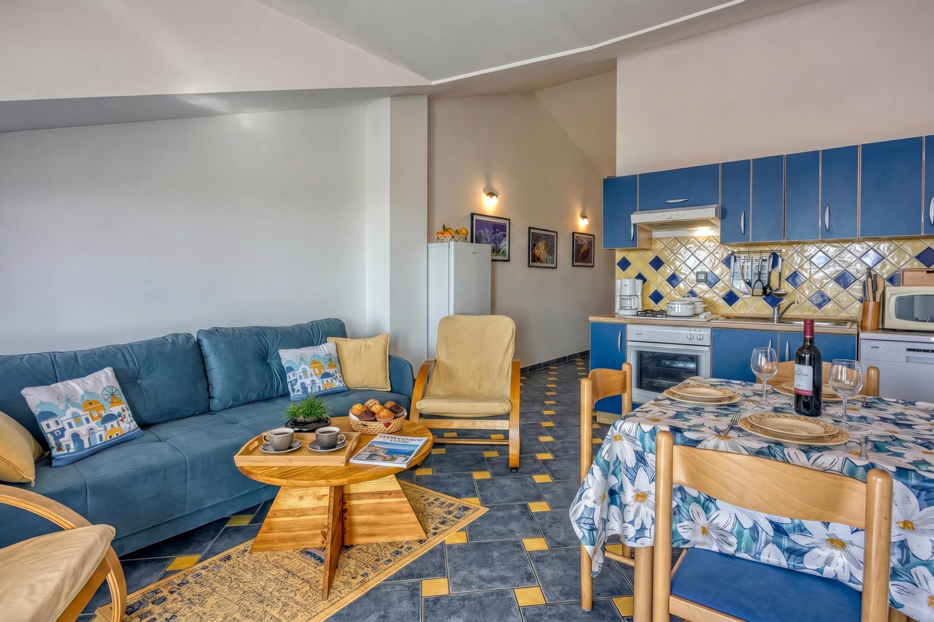 A compact living space with a sofa, armchair, dining table, and kitchenette.