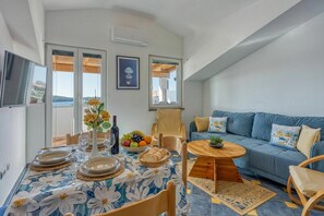 A modern living room with a dining area, a sofa set, and a view through large windows.