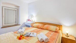 Une chambre d’hôtel comprenant un lit, une table de chevet avec une lampe, une fenêtre avec des stores et un petit bureau avec un miroir.