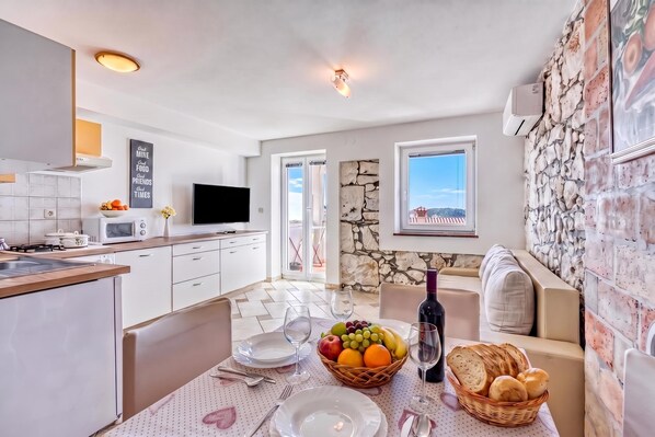 A modern kitchen with a dining area, a television, and a stone wall.