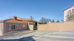 Un parking avec un bâtiment dont le toit est recouvert de tuiles et les murs sont de couleur beige.