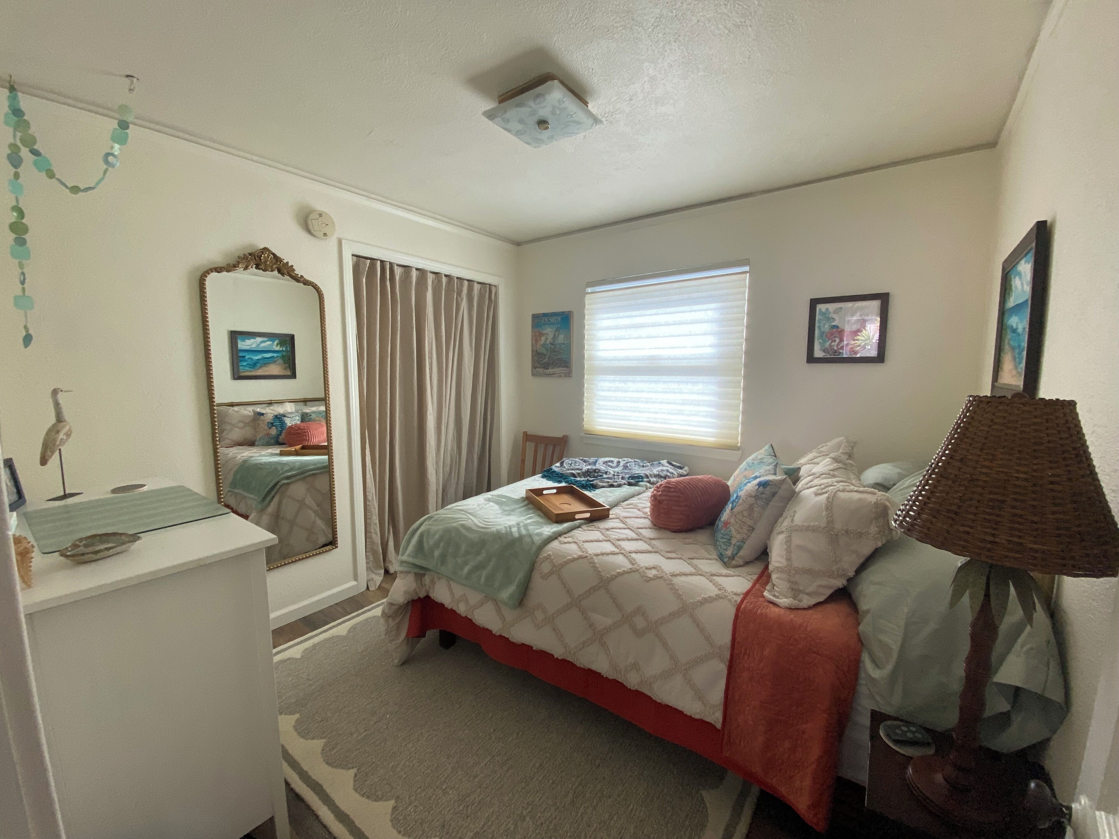 A bedroom with a bed, a dresser, a mirror, a window with blinds, and a lamp.