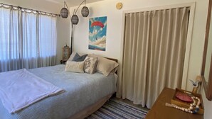 Un dormitorio con cama, cortinas, un cuadro, un reloj y una mesita de madera con un adorno.