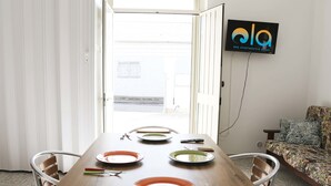 Ruokailutilassa on puinen pöytä, johon on katettu neljälle, tuolit, seinällä oleva televisio ja taustalla oleva sohva.