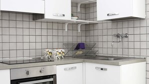 Moderni keittiö, jossa on valkoiset kaapit, sisäänrakennettu uuni ja ruostumattomasta teräksestä valmistettu allas.