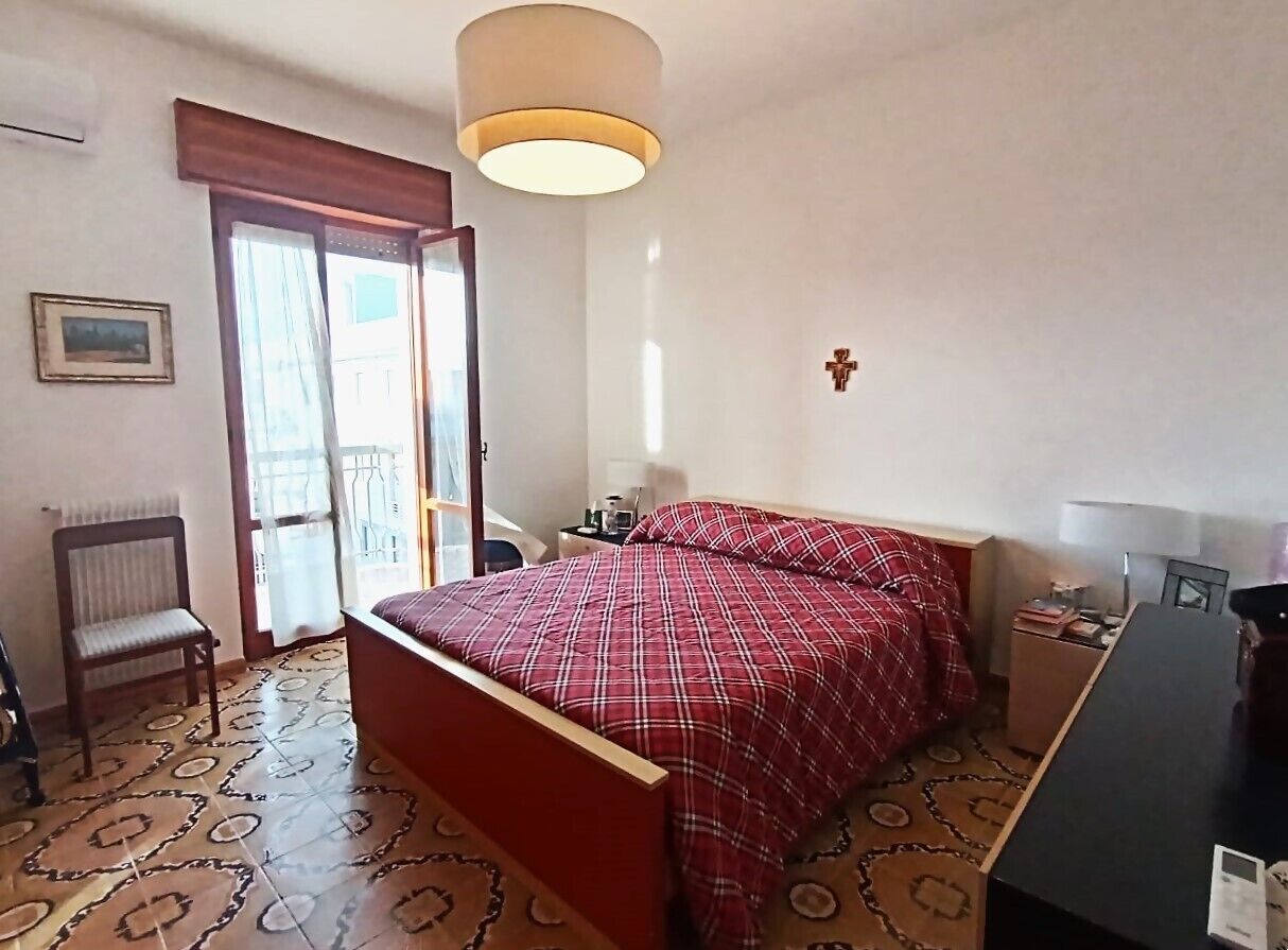 Een slaapkamer met een bed, een bureau, een stoel, een radiator en een deur die leidt naar een balkon.