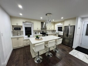 Una cocina moderna con armarios blancos, una isla central con taburetes de bar, electrodomésticos de acero inoxidable y una araña.
