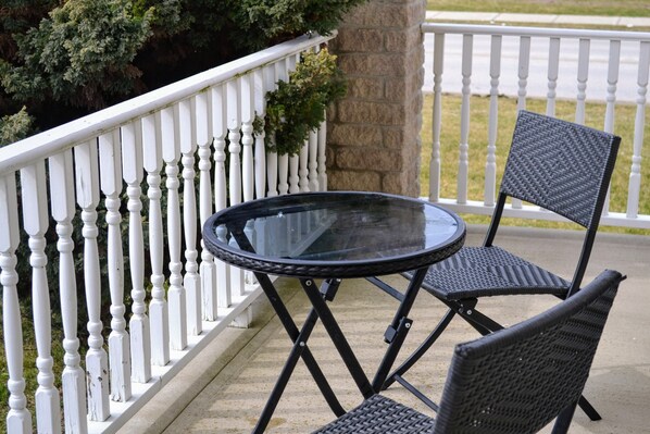 A black metal table and two wicker chairs on a concrete patio with a white railing.