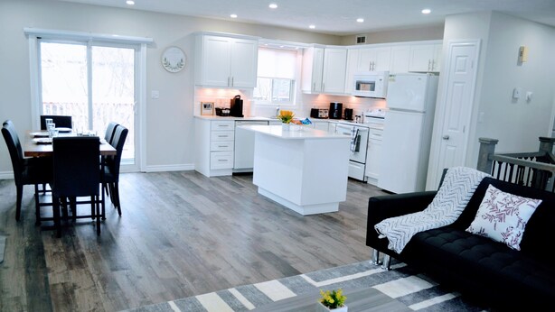 A modern kitchen with white cabinets, a central island, and a dining area with a table and chairs.