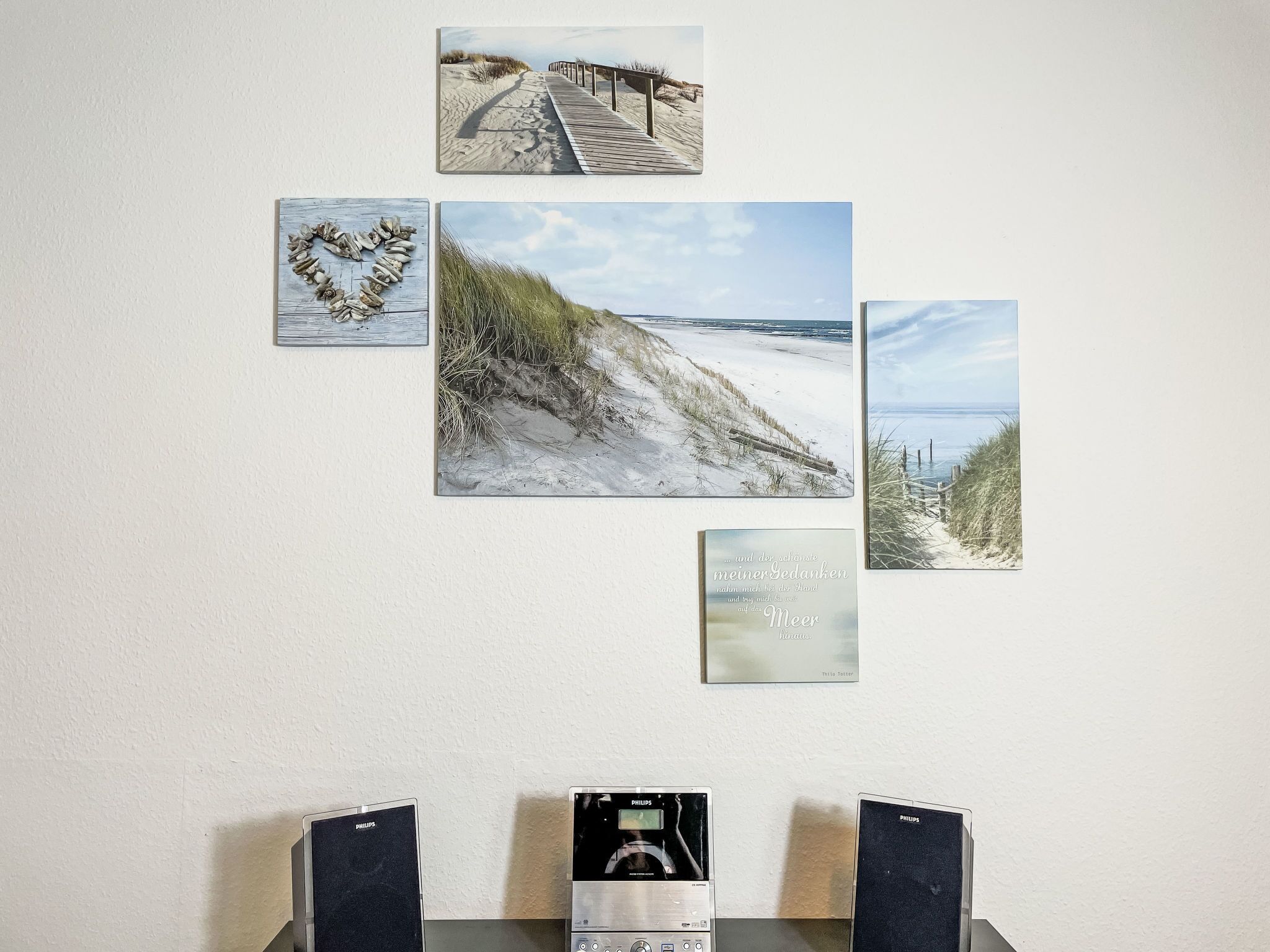A wall with four framed beach scenes and two Philips speakers.