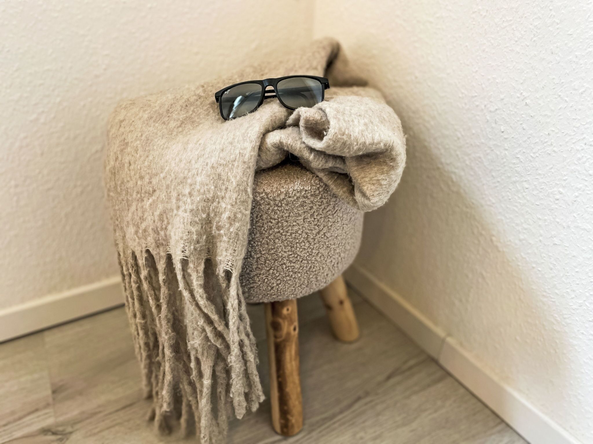 A corner with a small stool covered in a beige blanket, a pair of sunglasses on top, and a wooden leg.
