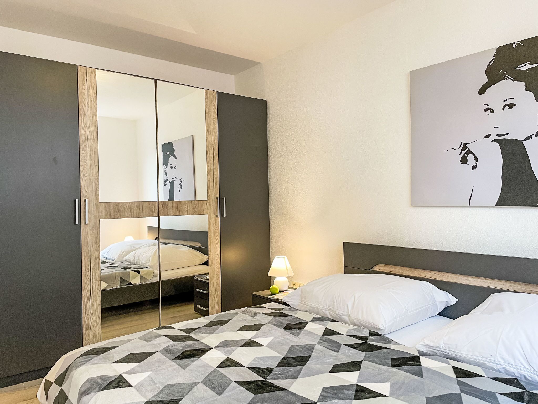 Une chambre moderne avec un lit, une armoire avec un miroir et une œuvre d’art accrochée au mur.