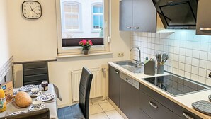 Cocina compacta con ventana, un reloj y zona de comedor con una mesa dispuesta para dos.