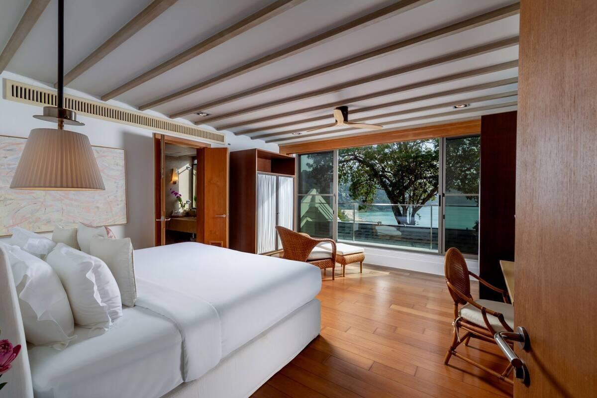 A modern bedroom with a large bed, a wooden ceiling, and a view of the outdoors.