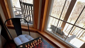 Une pièce avec un jeu d’échecs installé sur une table, une chaise et une fenêtre donnant sur des arbres.