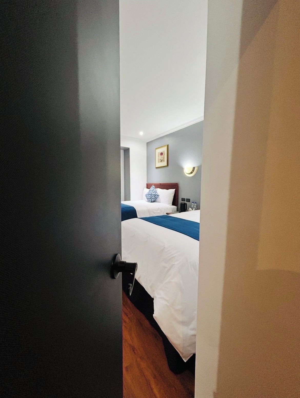 A hotel room with a bed, a bedside table, and a wall-mounted light fixture.