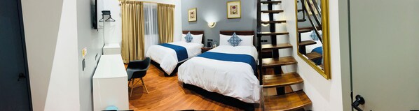 A hotel room with two beds, a desk, a chair, a staircase, and a mirror.