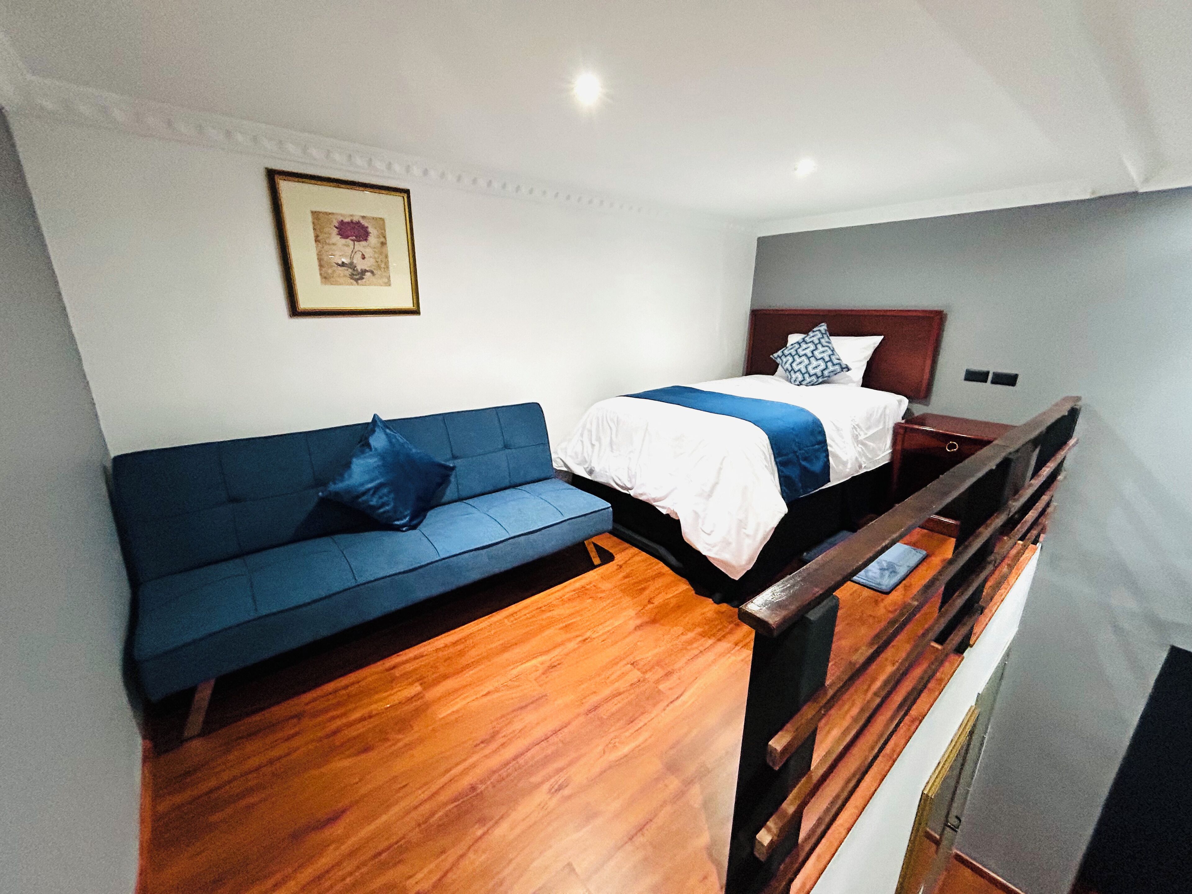 A hotel room with a blue sofa, a bed with a white and blue bedspread, and a wooden floor.