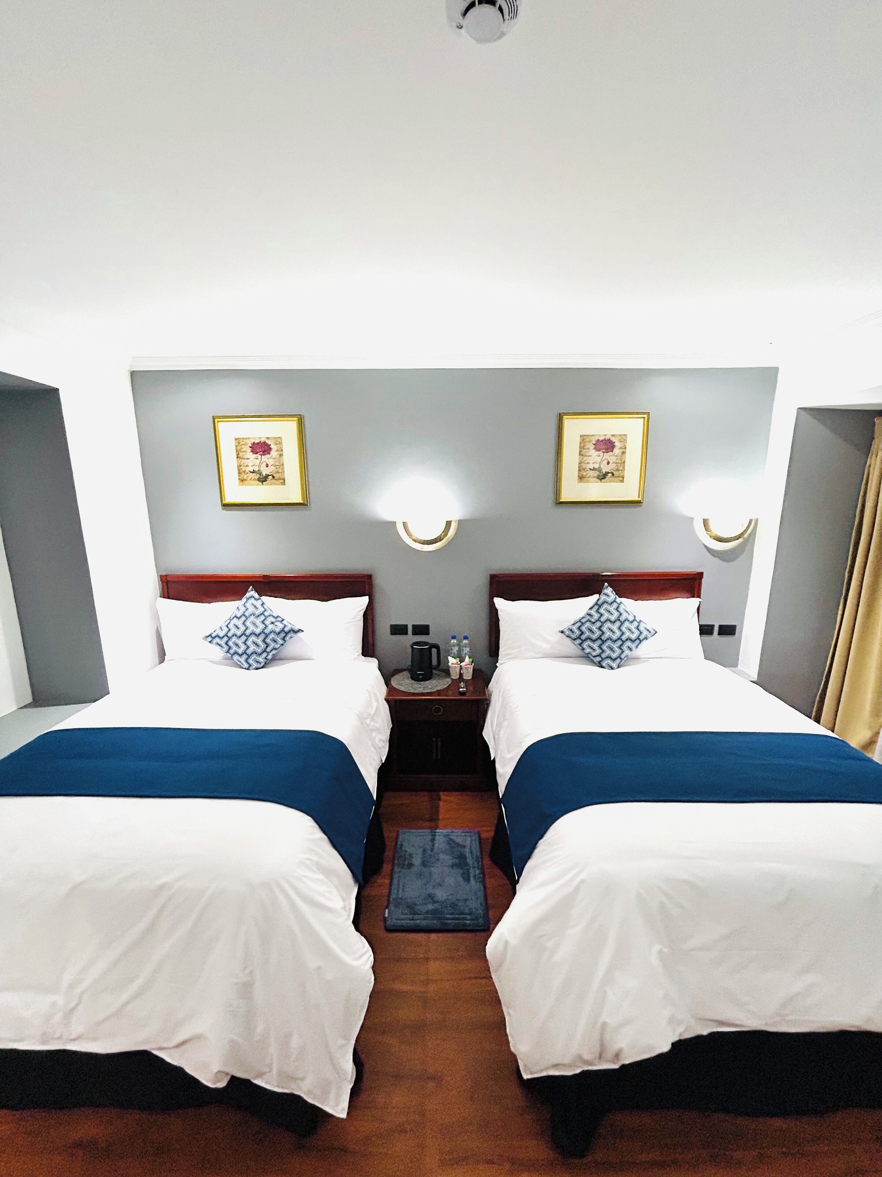 Een hotelkamer met twee bedden, een nachtkastje, lijstwerk en een plafondlamp.
