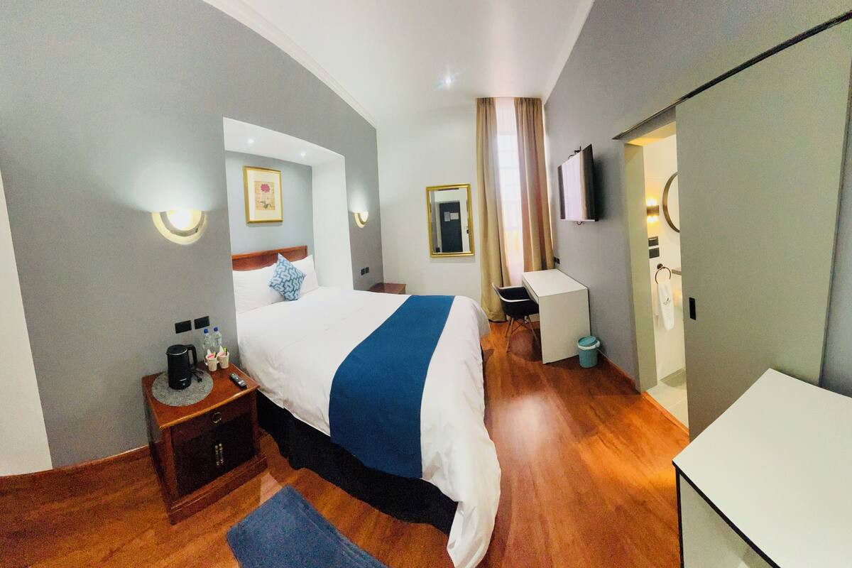 Een hotelkamer met een bed, nachtkastje, lamp en een klein bureau met stoel.