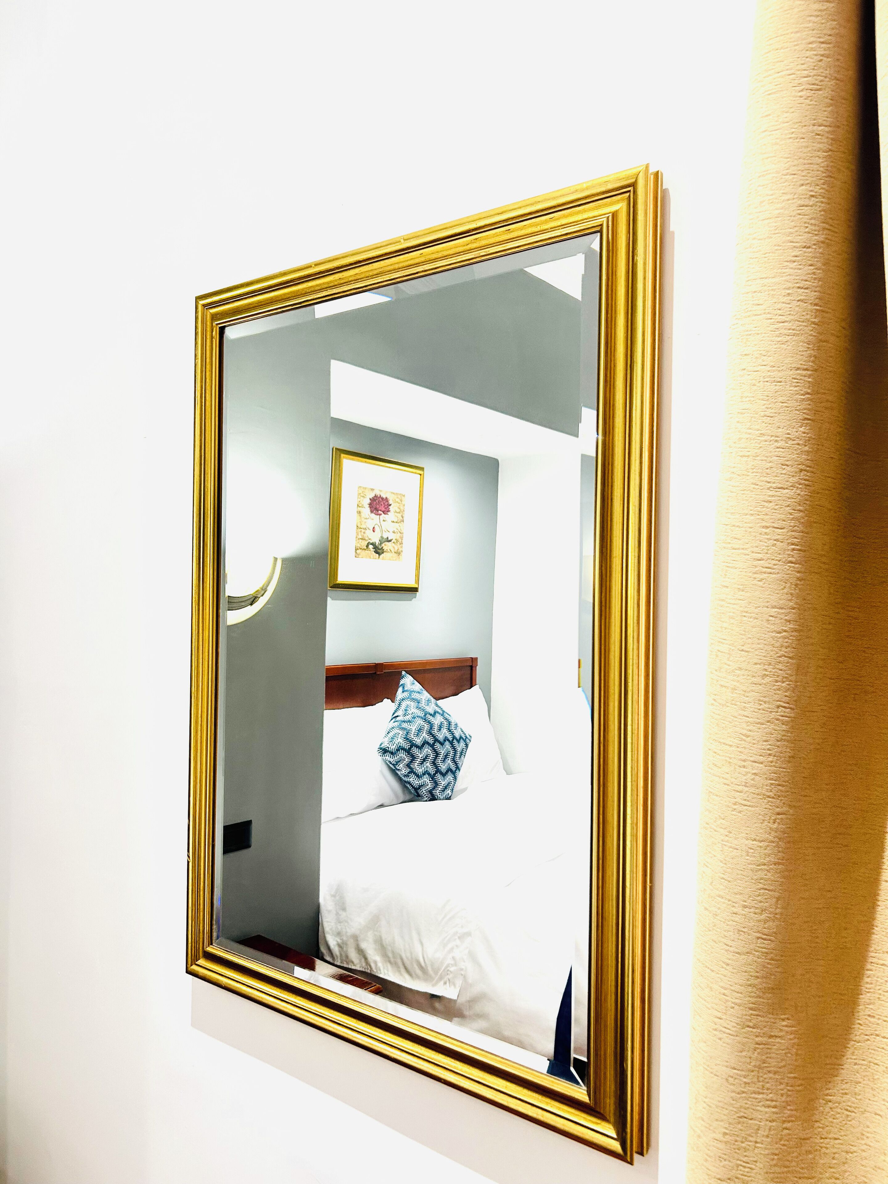 A hotel room with a bed, a bedside table, a wall-mounted mirror, and a framed picture on the wall.