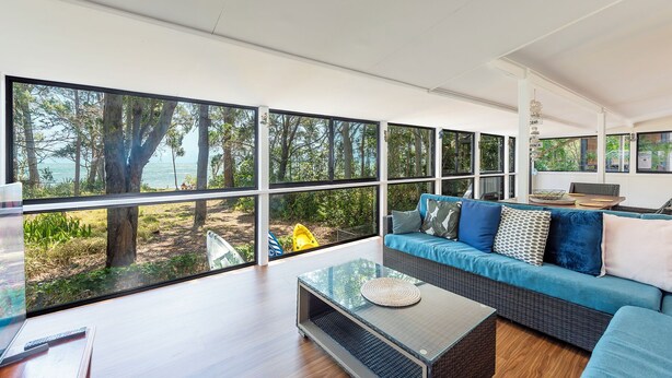 Ein modernes Wohnzimmer mit großen Fenstern, einem blauen Sofa und einem Glastisch.