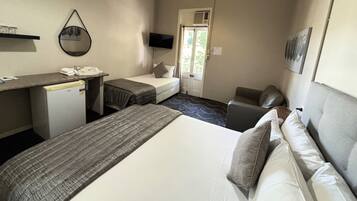 Habitación de hotel con cama, escritorio con teléfono, refrigerador pequeño, televisión y puerta que da a un balcón.