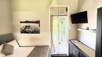 Ett sovrum med en säng, ett skrivbord, en tv och en dörr som leder ut till en balkong.