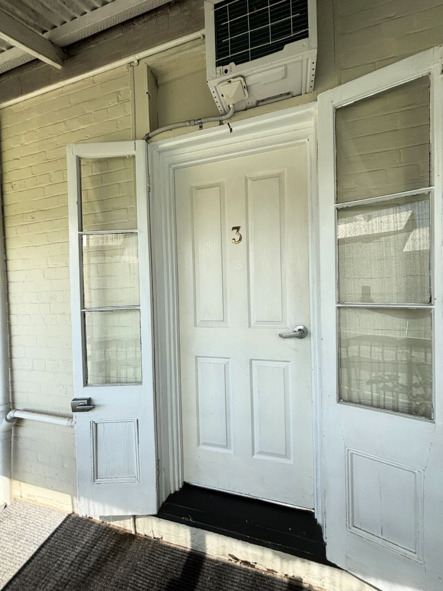 A white door with a number 3, a glass door with a metal handle, and an air conditioning unit above.
