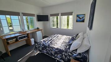 Ein Schlafzimmer mit einem Bett, einem Schreibtisch, einem Fernseher und großen Fenstern.