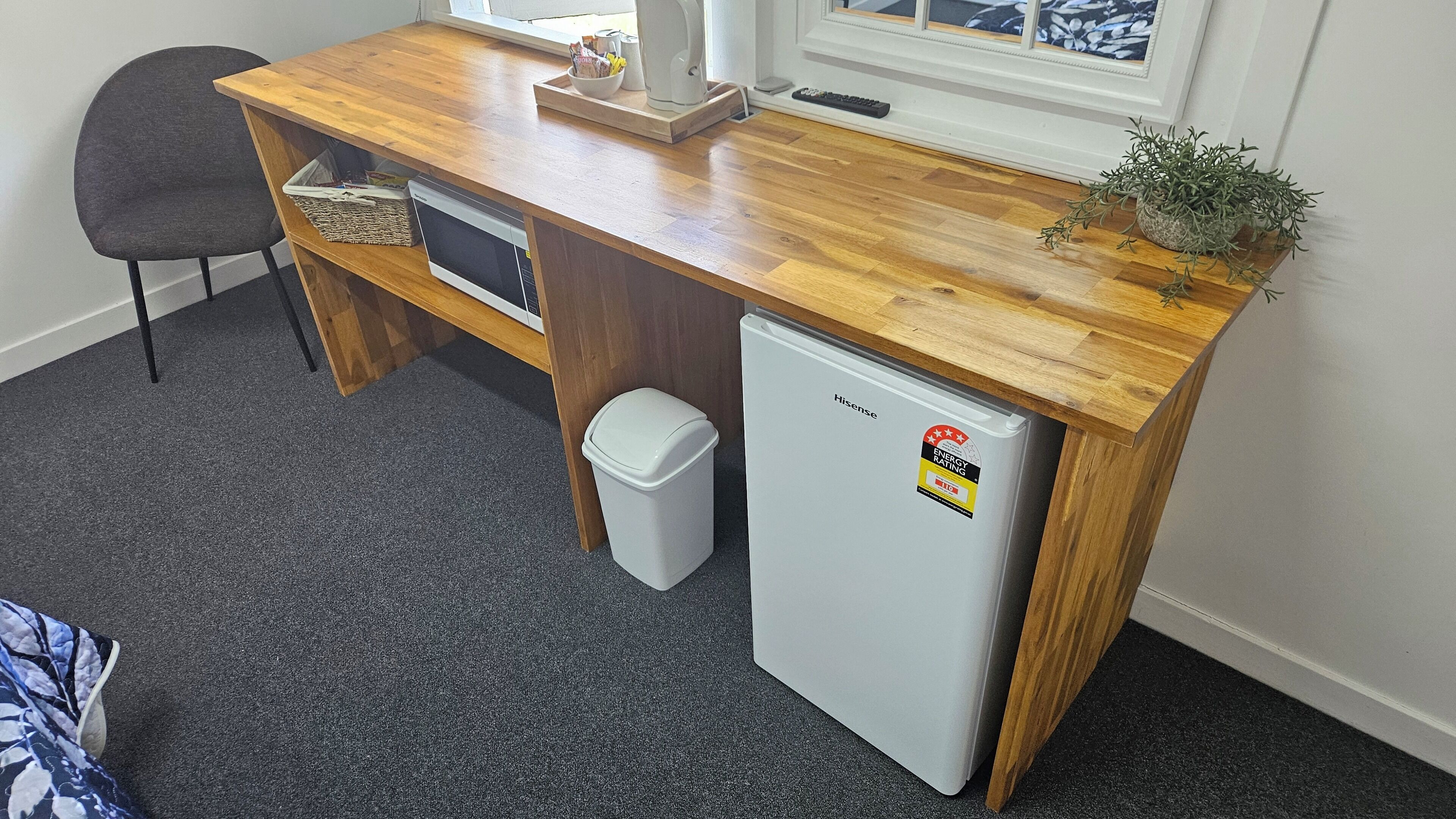A compact kitchenette with a wooden countertop, a built-in dishwasher, a small refrigerator, and a waste bin.
