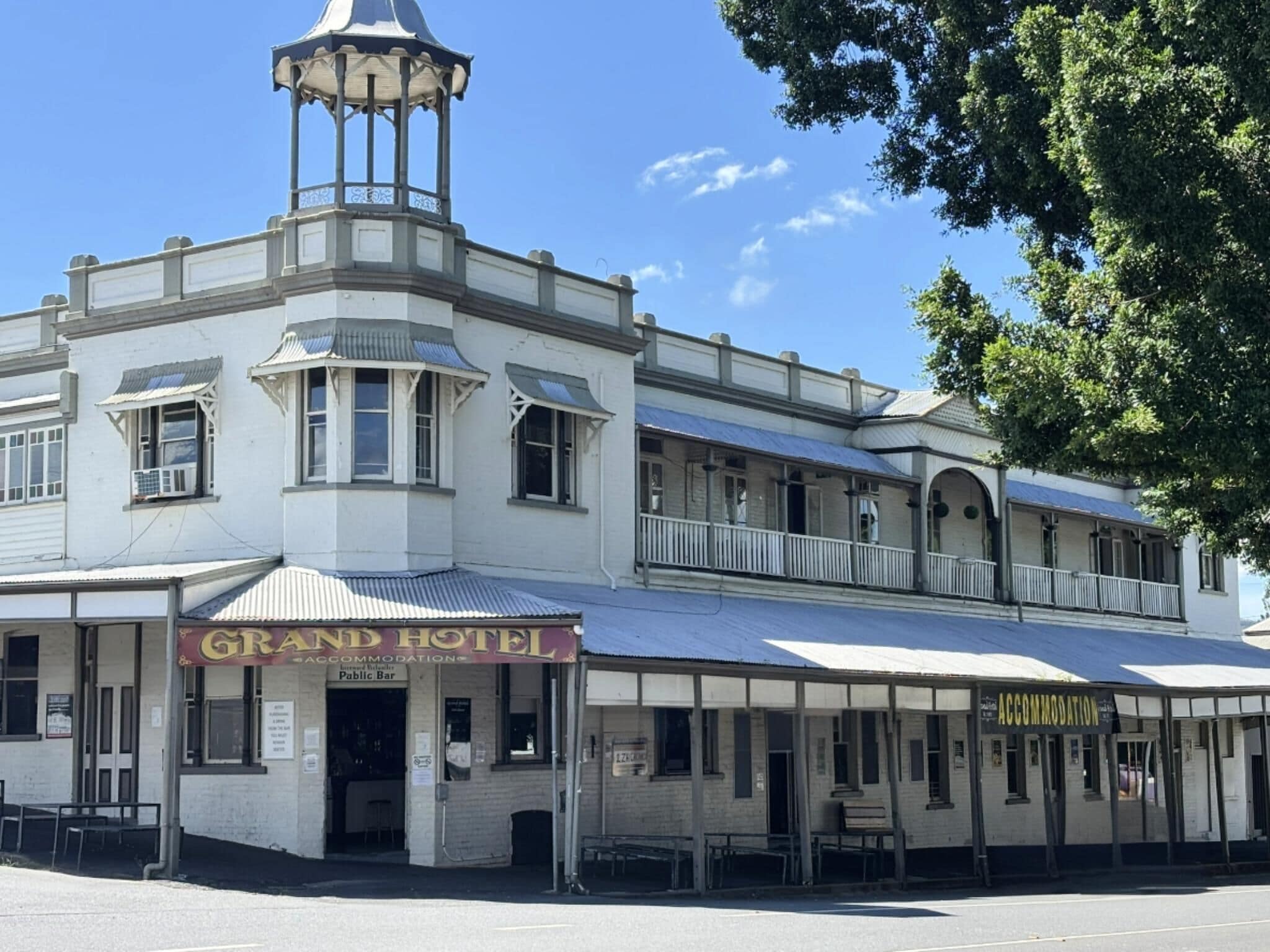 A two-story building with a prominent corner tower and a balcony. The ground floor has a sign for 'Grand Hotel' and a 'Public Bar'.