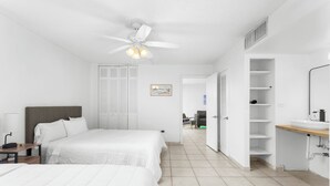 A hotel room with two beds, a ceiling fan, a bathroom with a sink and mirror, and a hallway leading to another room. - Bay Harbor Sunset Apt 3A (Bay Harbor Islands)