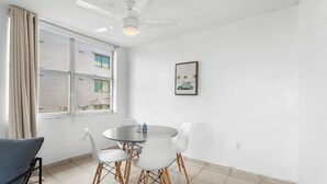 A dining area with a round table, white chairs, a ceiling fan, and a window with curtains. - Bay Harbor Sunset Apt 3A (Bay Harbor Islands)
