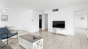 A modern living room with a sofa, coffee table, TV, and white cabinetry. - Bay Harbor Sunset Apt 3A (Bay Harbor Islands)
